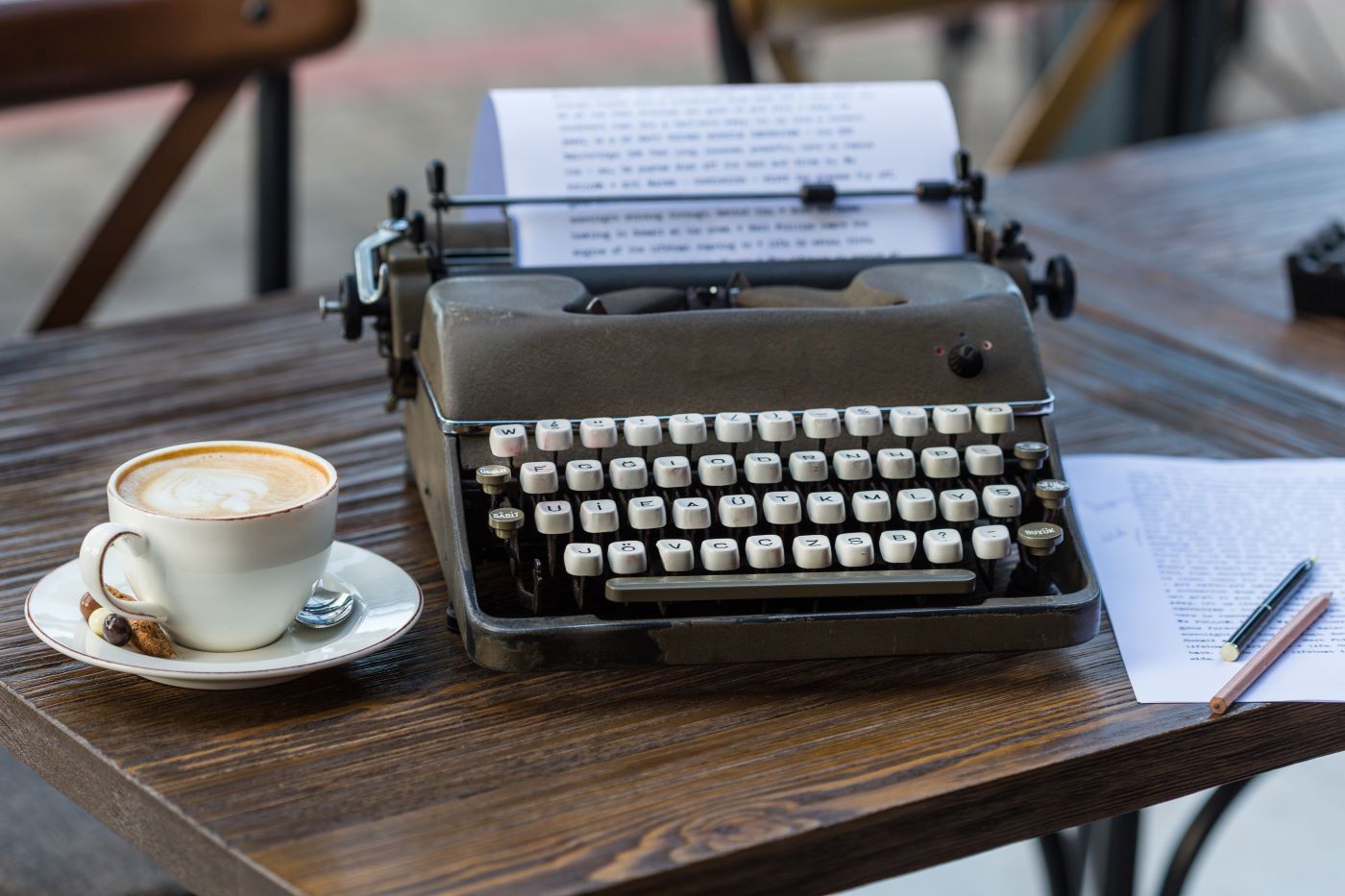 retro typewriter, paper with pencils and a cup of cappuccino on wooden table